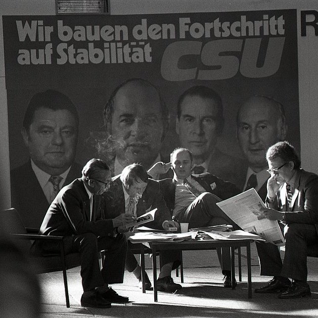 Teilnehmer am CSU-Parteitag vom 3./4.11.1972 in München vor dem Wahlplakat „Wir bauen den Fortschritt auf Stabilität CSU“ mit den Porträts der CDU/CSU-Politiker Franz Josef Strauß, Rainer Barzel, Gerhard Schröder, Hans Katzer